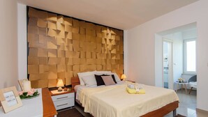 Ein modernes Schlafzimmer mit einem Holz-Kopfteil, einem großen Bett mit einer beigen Bettdecke, Nachttischen mit Lampen und einem kleinen Tisch mit einem gerahmten Bild und Blumen.