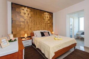 Ein modernes Schlafzimmer mit einem Holz-Kopfteil, einem großen Bett mit einer beigen Bettdecke, Nachttischen mit Lampen und einem kleinen Tisch mit einem gerahmten Bild und Blumen.
