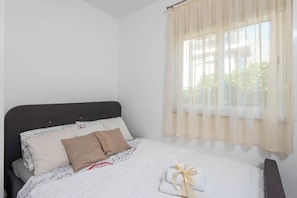 A neatly made bed with a patterned bedspread, a dark headboard, and a window with sheer curtains. - Apartments Lenka (Orebic)