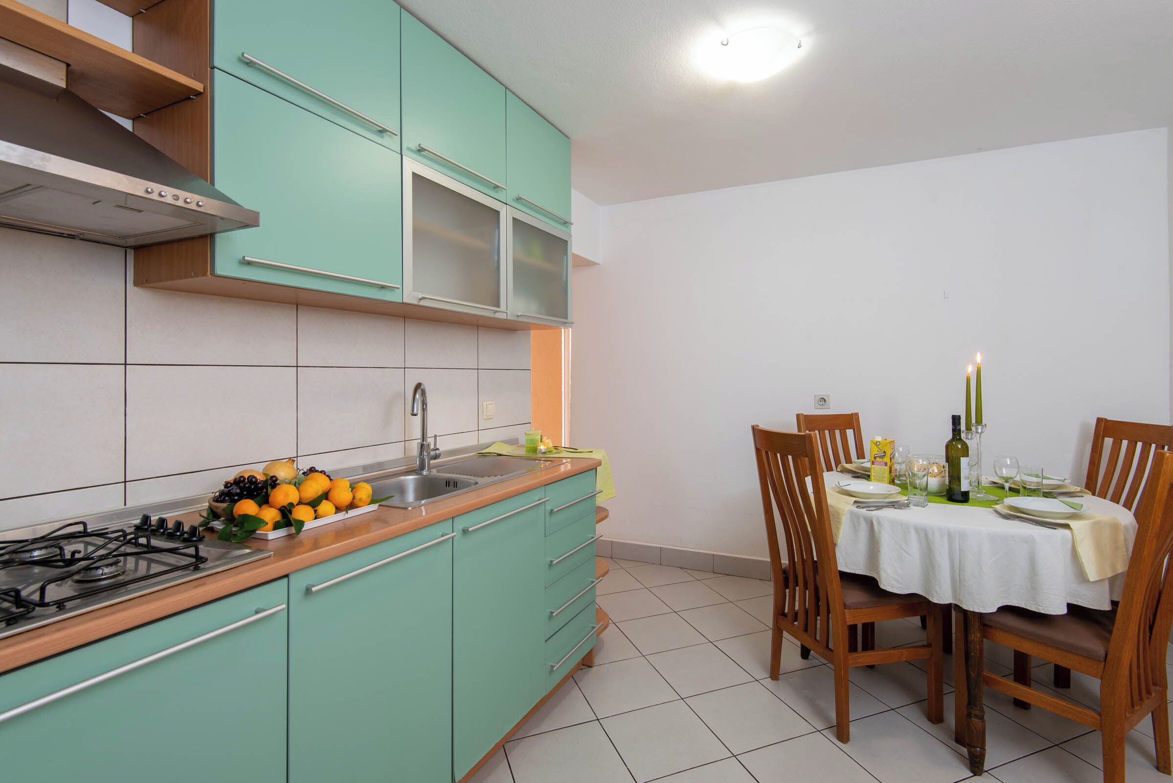 Une cuisine avec des meubles de couleur turquoise, une cuisinière à gaz et un coin repas avec une table dressée pour quatre personnes.