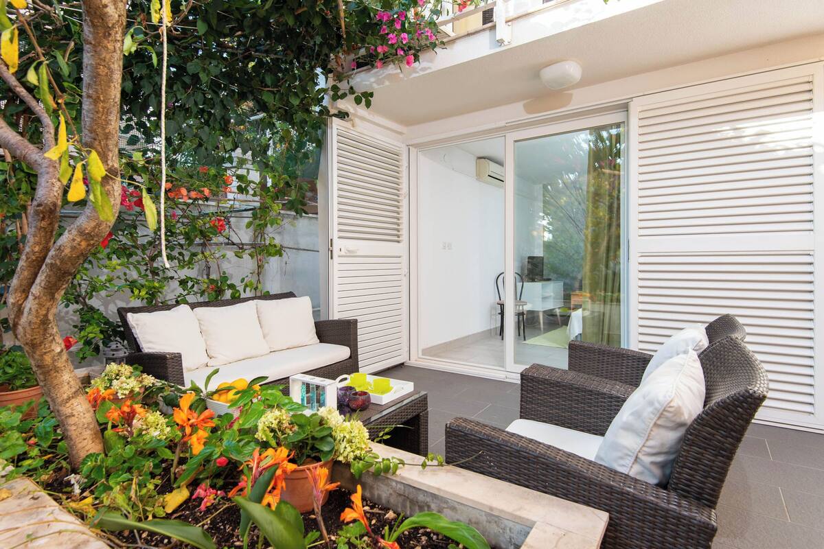 A patio area with wicker furniture, a white sofa, and a dining table. There is a glass door leading to an indoor space.