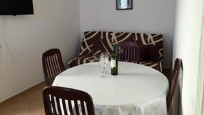 Een eetgedeelte met een ronde tafel, stoelen, een bank en een fles wijn.