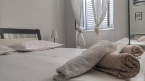 Een net opgemaakt bed met witte en beige handdoeken, een bedlampje en een raam met gordijnen.