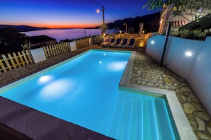 A rectangular swimming pool with a stone border, surrounded by a low stone wall and a wooden fence. - House Rovana (Jasenice)