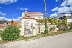 A two-story stone house with a red-tiled roof, a gated entrance, and a small porch. - House Rovana (Jasenice)