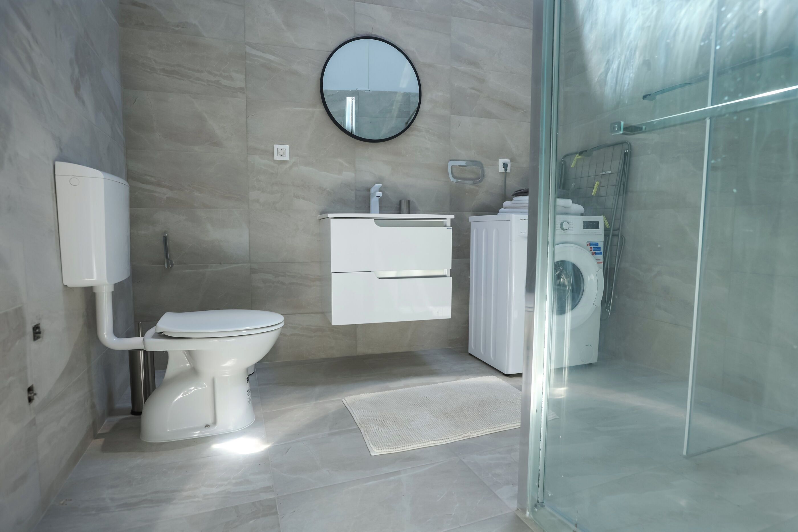 A modern bathroom with a toilet, sink, mirror, and a glass shower enclosure.