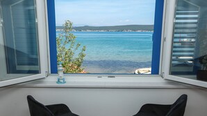 A room with a view of a calm sea and distant hills. There are two black chairs in the foreground. - Apartments Seafront (Pasman)