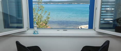 A room with a view of a calm sea and distant hills. There are two black chairs in the foreground.
