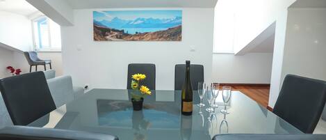Un comedor moderno con una mesa de vidrio, sillas negras, una planta en maceta con girasoles, una botella de vino y copas de vino.