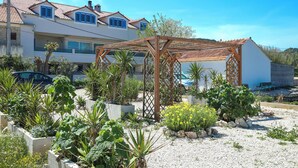A residential building with a garden area featuring plants and a wooden pergola. - Apartments Seafront (Pasman)