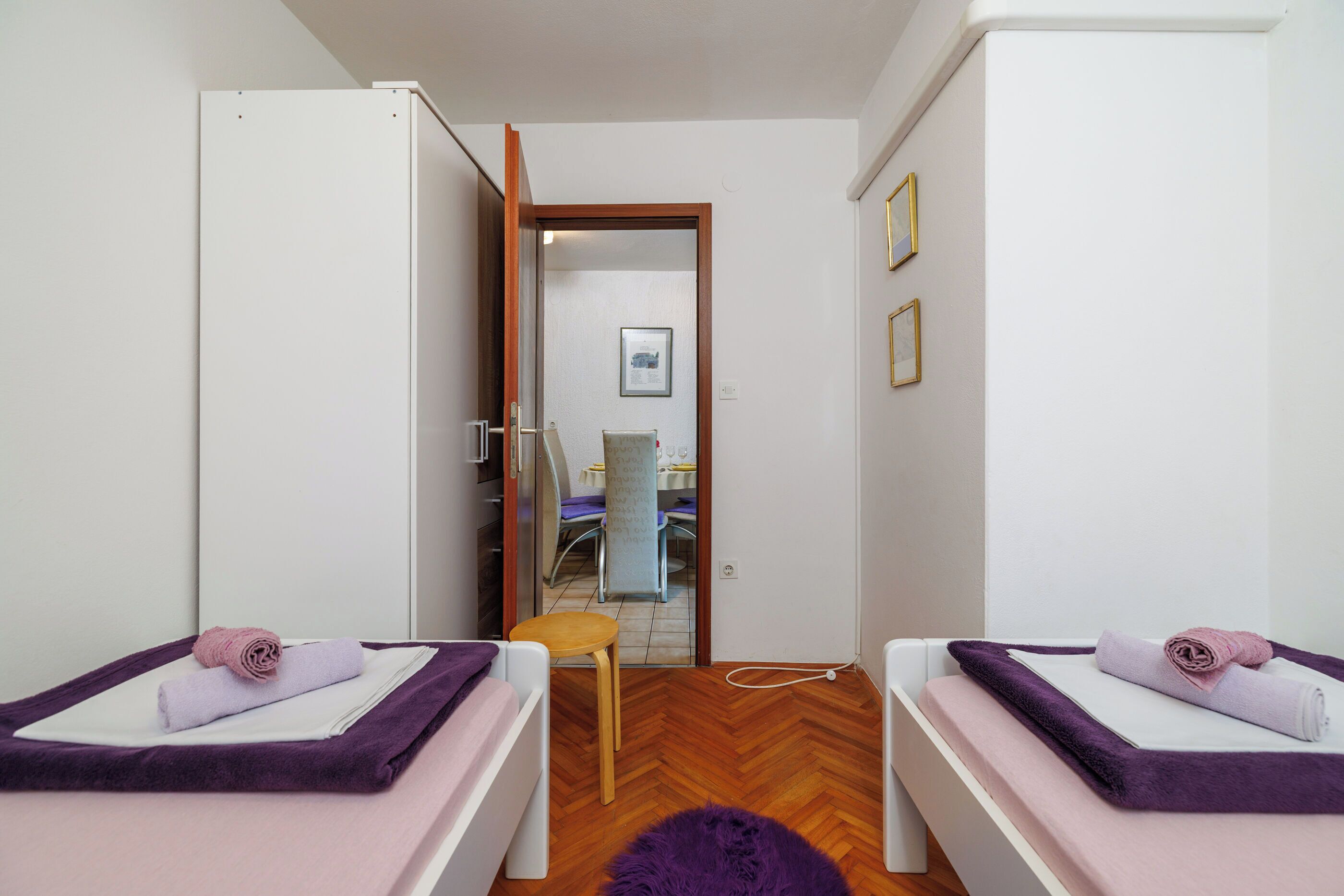 Een kamer met twee bedden, elk voorzien van een paarse deken en een opgerolde handdoek. Er staat een houten stoel en een kleine tafel in het midden.