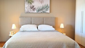 Una cama bien hecha con un edredón acolchado, dos lámparas de noche y una obra de arte enmarcada con hojas en la pared.