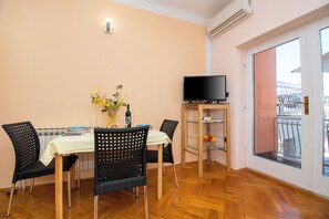 A dining area with a table set for two, a television on a stand, and a balcony with a railing. - Apartments and Room Agiss With Pool (Vodice)