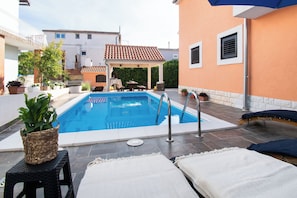 A swimming pool with lounge chairs and a covered seating area. - Apartments and Room Agiss With Pool (Vodice)
