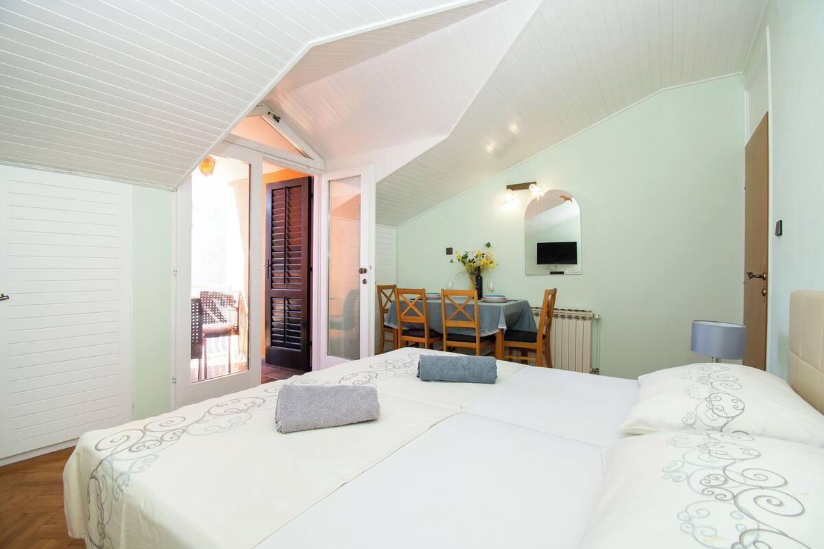 Un dormitorio con una cama grande, una mesa de comedor y una silla al fondo.