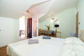 A bedroom with a large bed, a dining table, and a chair in the background. - Apartments and Room Agiss With Pool (Vodice)