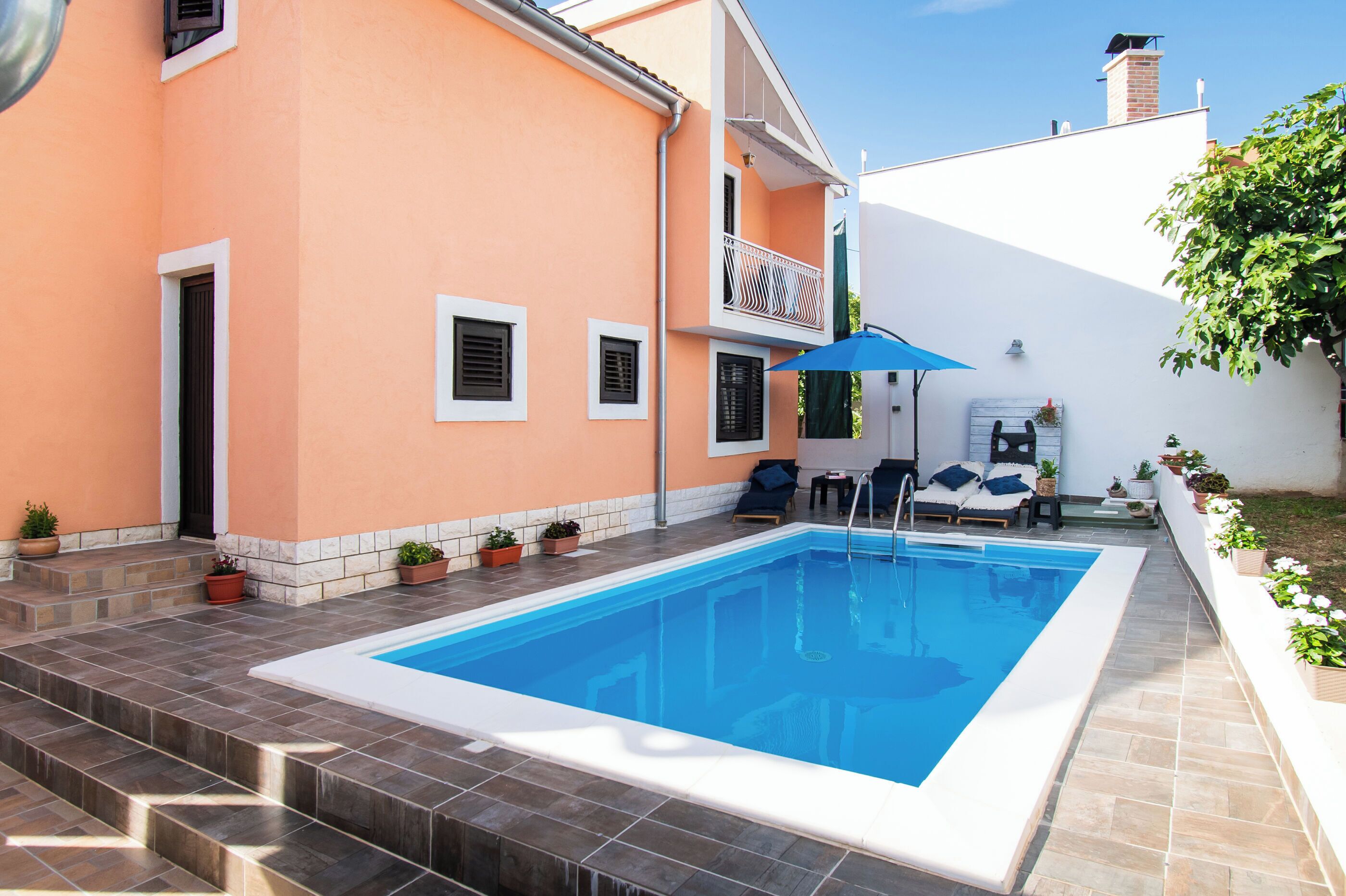 En swimmingpool med fliseterrasse, en lille balkon med gelænder og plantekasser.