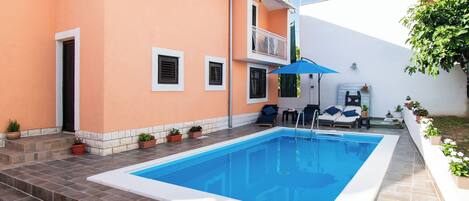 En swimmingpool med fliseterrasse, en lille balkon med gelænder og plantekasser.