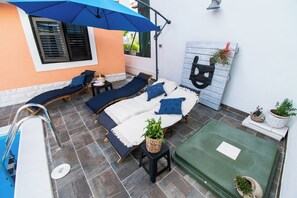 A sunlit patio with two lounge chairs, a small table, and a blue umbrella. - Apartments and Room Agiss With Pool (Vodice)