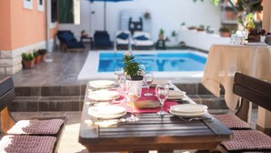 A dining table set for two with a pool in the background. - Apartments and Room Agiss With Pool (Vodice)