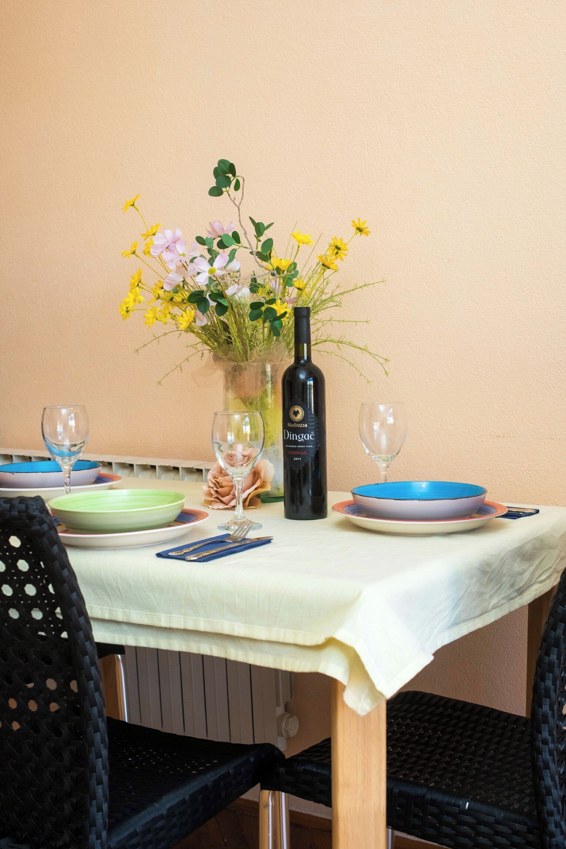Un tavolo imbandito con piatti, una bottiglia di vino e un vaso di fiori.