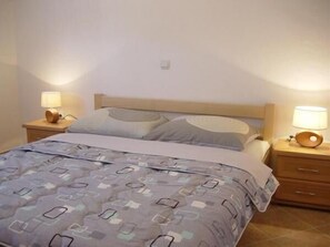 Un letto rifatto con cura, con copripiumino fantasia, due comodini con lampade e una testiera in legno.