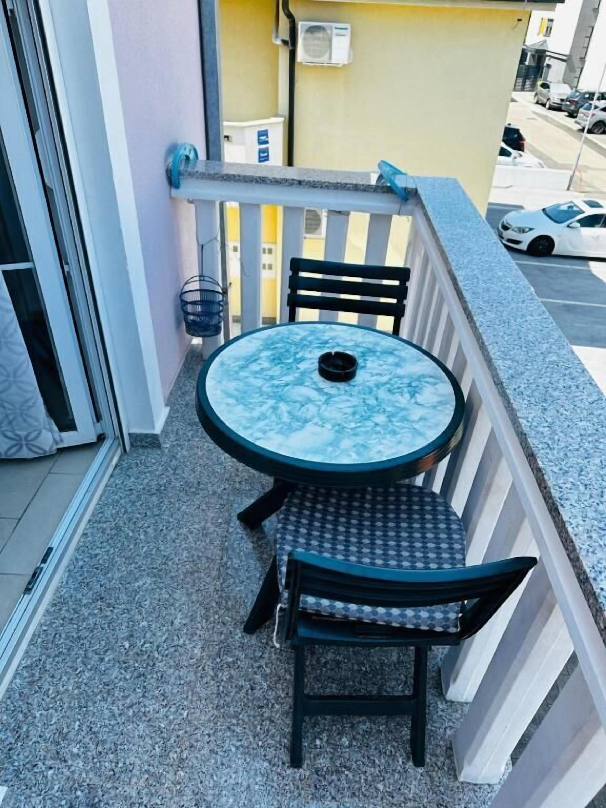 Un balcón con una mesa redonda y dos sillas, una cesta colgante pequeña y vista a la calle.