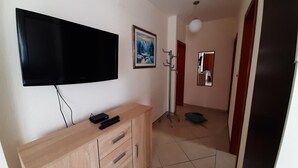 A room with a flat-screen TV mounted on the wall, a wooden cabinet with drawers, a painting, a coat rack, and a mirror. - Apartments Vladimir (Malinska-Dubasnica)