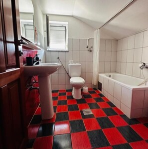 Un bagno con pavimento a scacchi rossi e neri, un water bianco, un lavandino e una vasca.