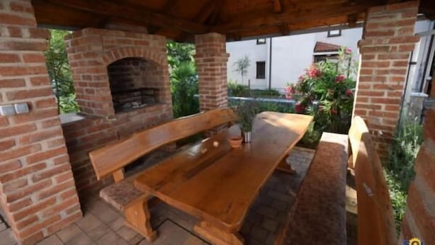 An outdoor patio with a brick oven, wooden benches, and a table. - Apartments Vladimir (Malinska-Dubasnica)