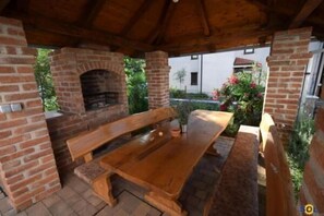 An outdoor patio with a brick oven, wooden benches, and a table. - Apartments Vladimir (Malinska-Dubasnica)