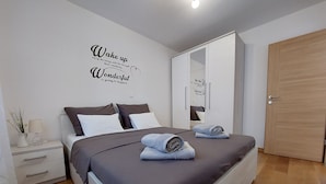 Une chambre moderne avec un lit, une table de chevet, une lampe et une citation inspirante sur le mur.