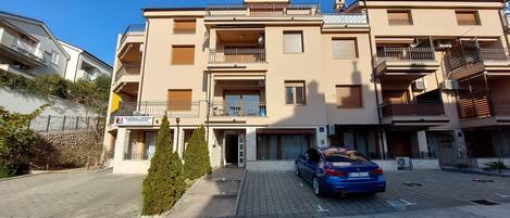 A multi-story residential building with balconies, a paved driveway, and a parked car.