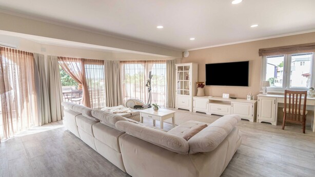 A spacious living room with a large beige sofa, a coffee table, and a TV mounted on the wall. - Apartments Vintage (Rab)
