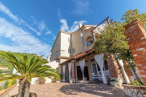 A two-story house with a stone facade, a balcony with white curtains, and a palm tree in the foreground. - Apartments Vintage (Rab)