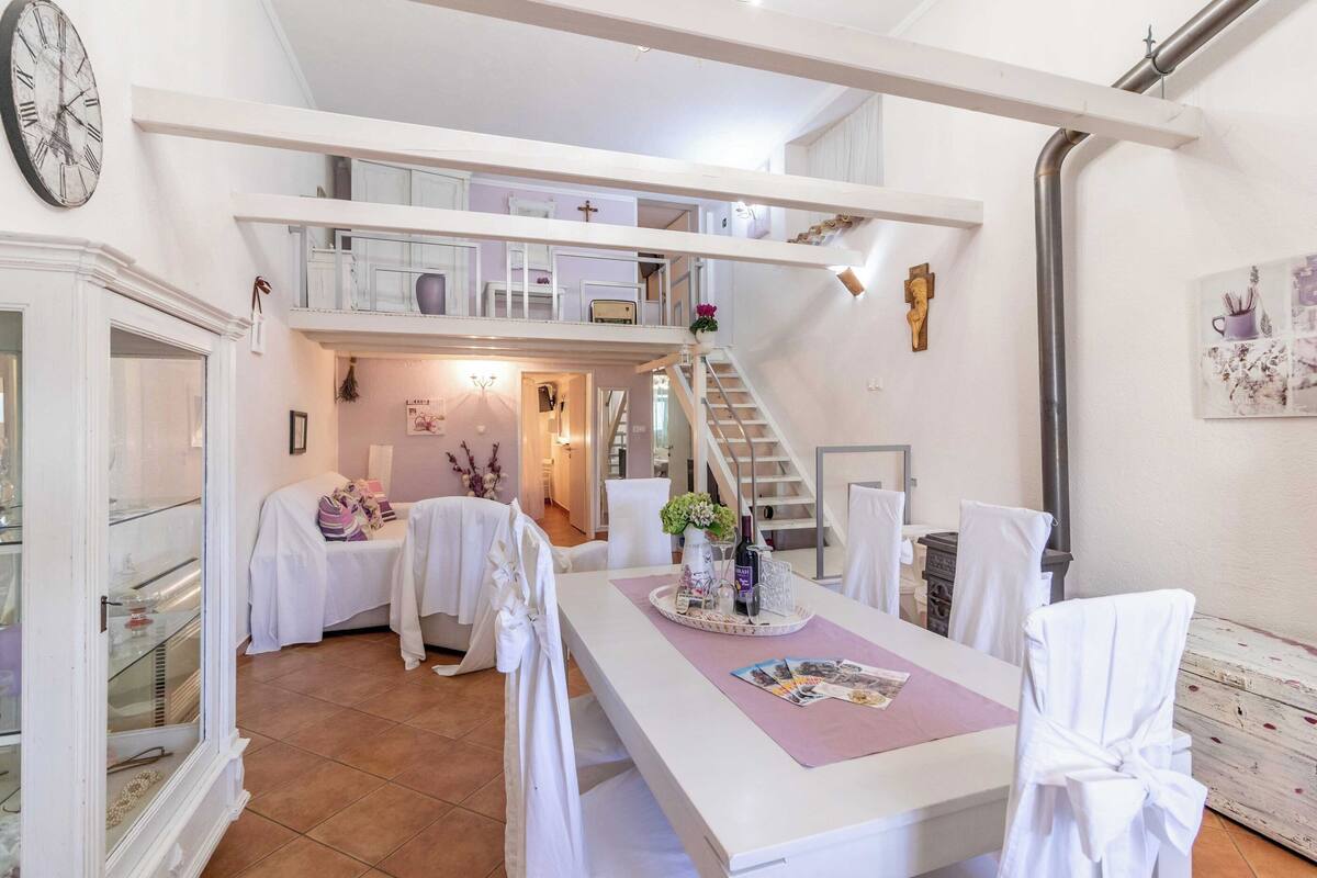 Une salle à manger spacieuse avec un plafond haut, un escalier menant à un niveau supérieur et une grande horloge au mur.