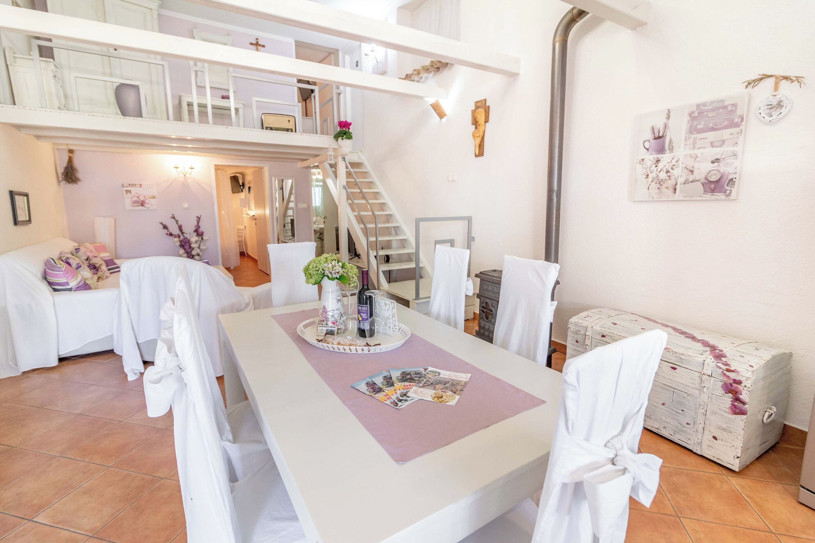 A spacious dining area with a high ceiling, a staircase leading to an upper level, and a white chest of drawers against the wall.