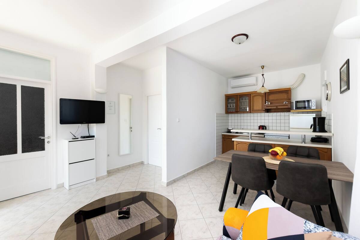 A modern kitchen with white cabinets, a microwave, and a dining area with a glass table and chairs.