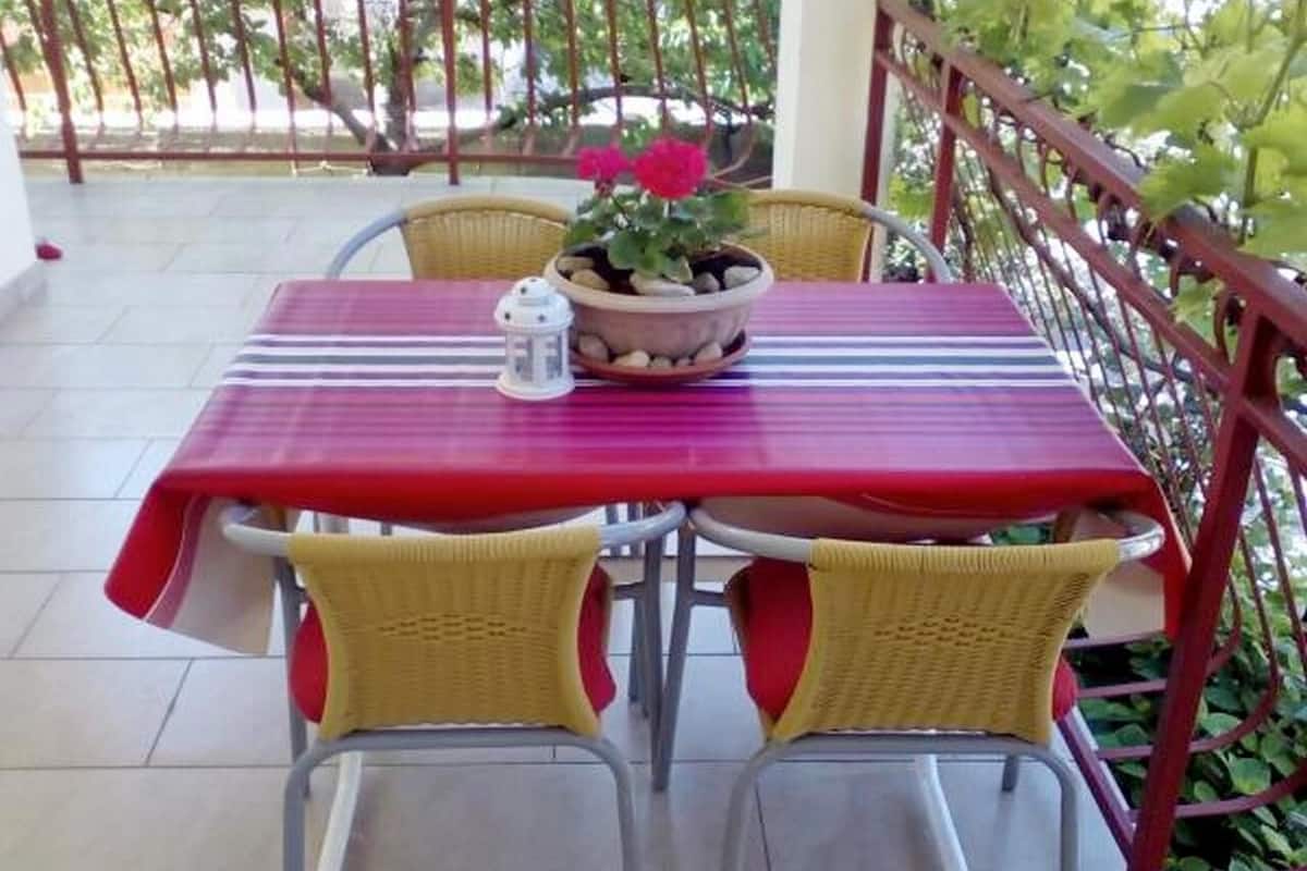 Ein Tisch mit rotem Tischtuch, zwei Korbstühle und ein Blumentopf mit roten Blüten.
