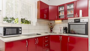 Une cuisine avec des meubles de couleur rouge, un four à micro-ondes, une cuisinière et une fenêtre ornée de rideaux en dentelle.