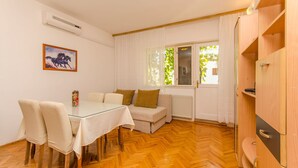 Un coin repas avec une table et des chaises en verre, un canapé avec des coussins, un radiateur et une fenêtre avec des rideaux.