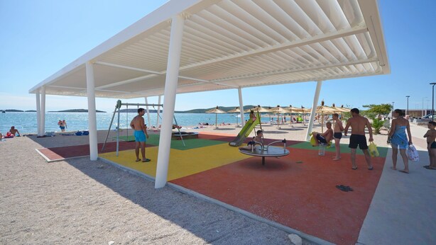 Une aire de jeux située au bord de la plage, avec un espace de repos abrité, des balançoires et un toboggan.