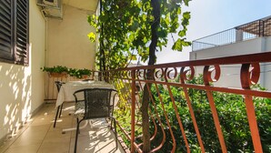 Un balcon avec une table et des chaises, un pot de fleurs et une rambarde en métal.