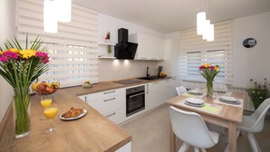 Eine moderne Küche mit weißen Schränken, einer Holzauskładung und einem Essbereich mit weißen Stühlen und einem Tisch für zwei Personen.