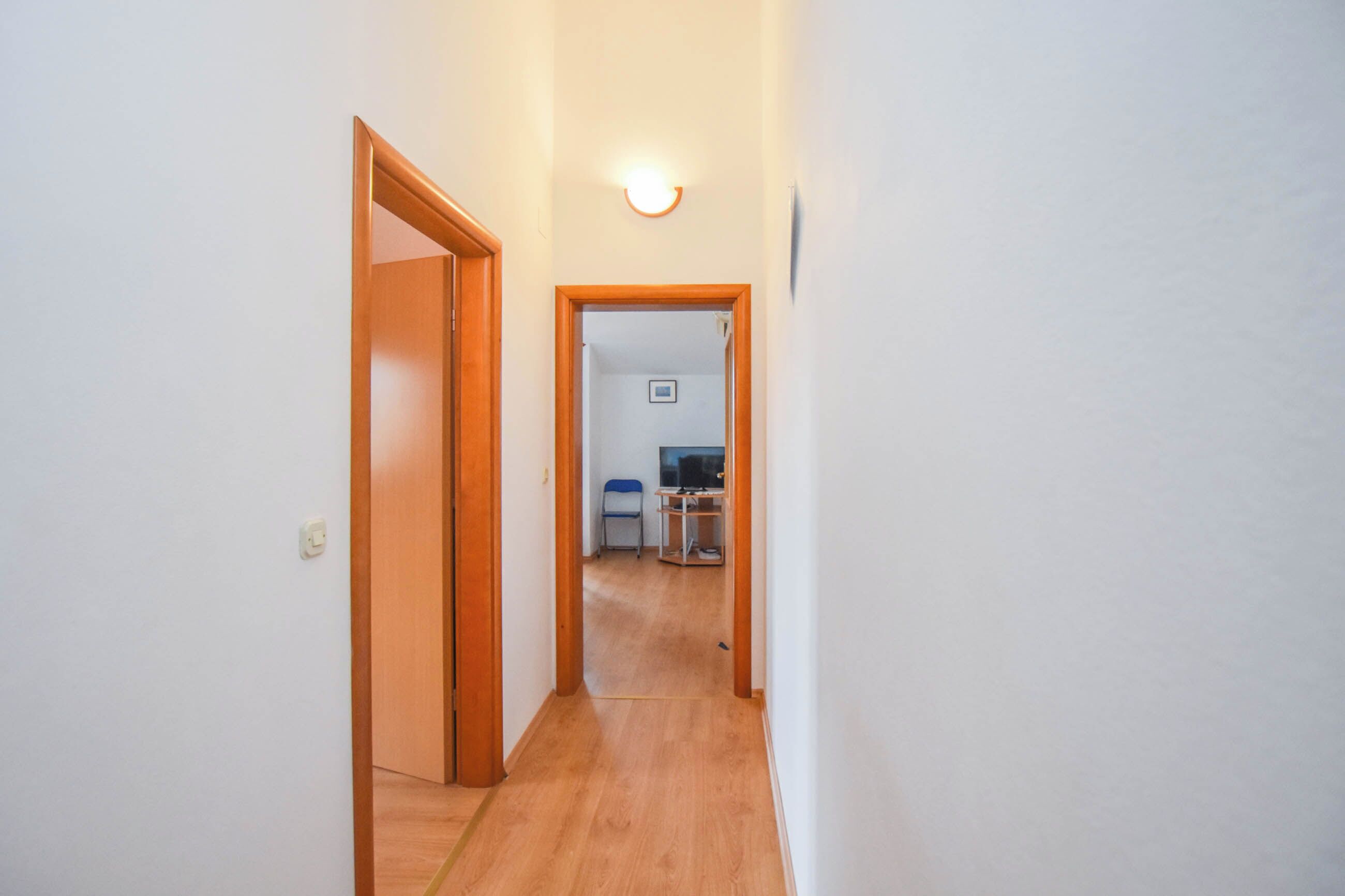 A narrow hallway with wooden flooring and white walls.