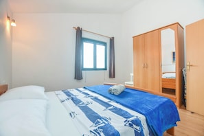 A bedroom with a bed, a wardrobe, a window with curtains, and a bedside table. - Apartments Studenac (Tkon)