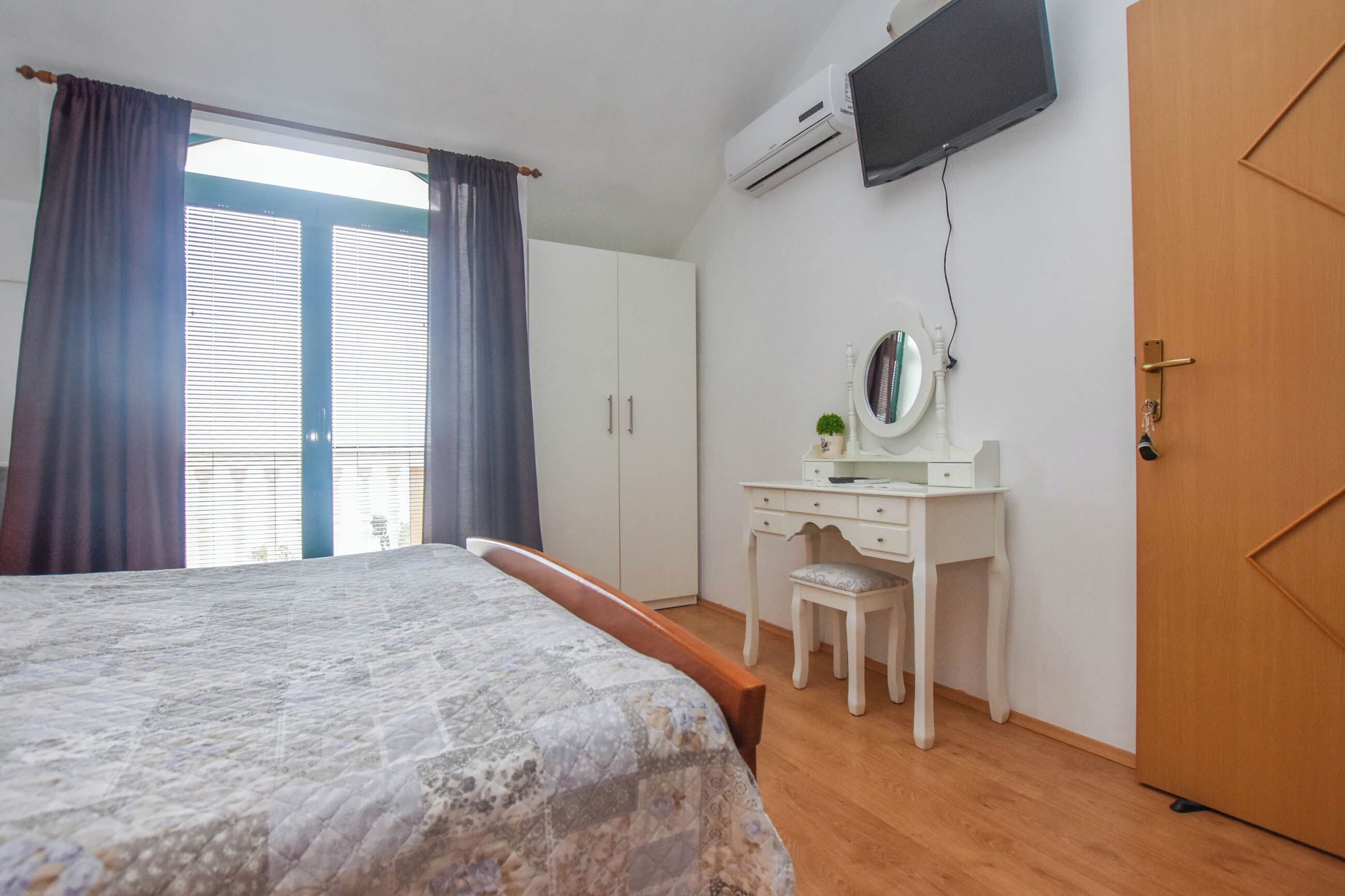 A bedroom with a bed, a desk with a chair, a television, and a wardrobe.