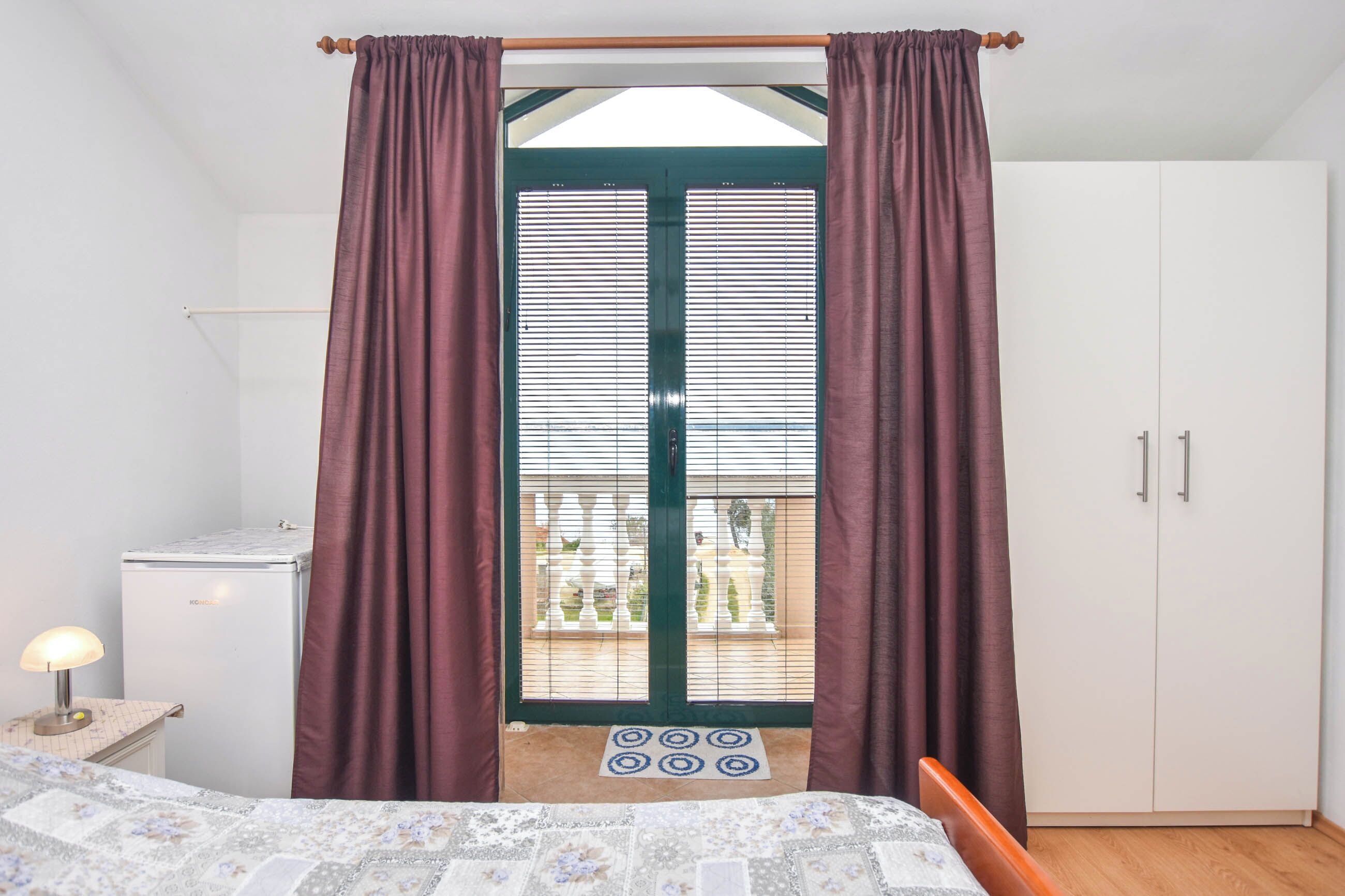 A bedroom with a bed, a nightstand, a wardrobe, and a view through a door with curtains.