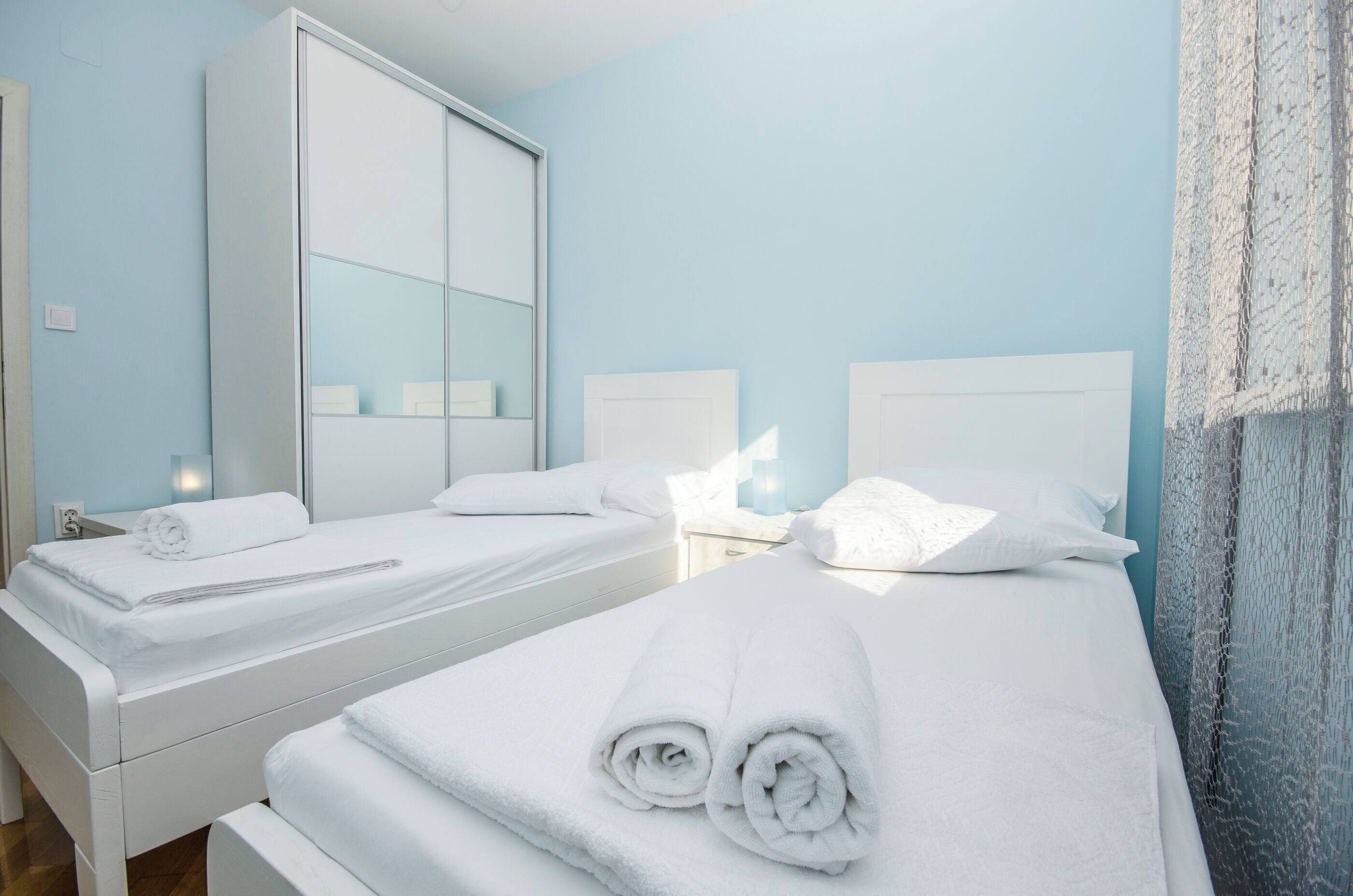 A hotel room with two beds, white linens, a large mirror, and a light blue wall.