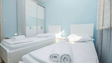 A hotel room with two beds, white linens, a large mirror, and a light blue wall.